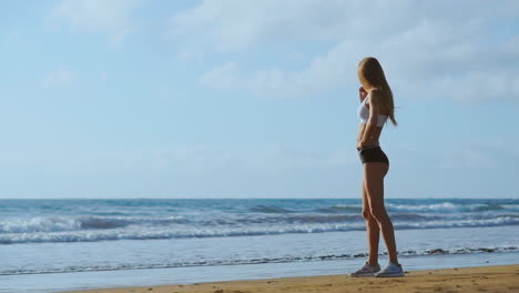 Girl's-legs-in-sports-clothes-standing-near-the-ocean-and-touching-her-hair-in-slow-motion.